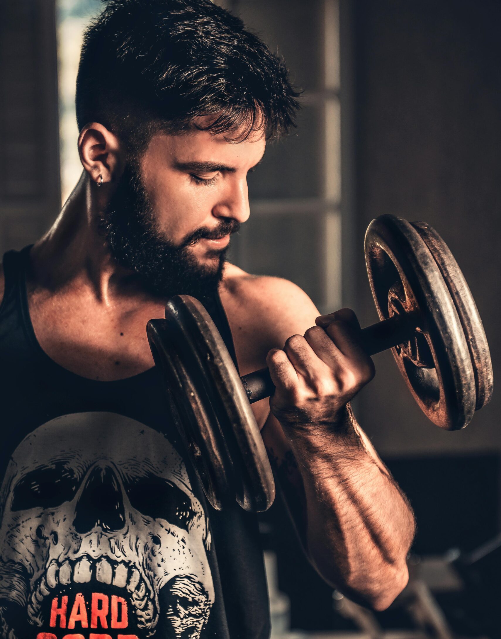 Bearded man in gym lifting a heavy dumbbell, showcasing strength and fitness.